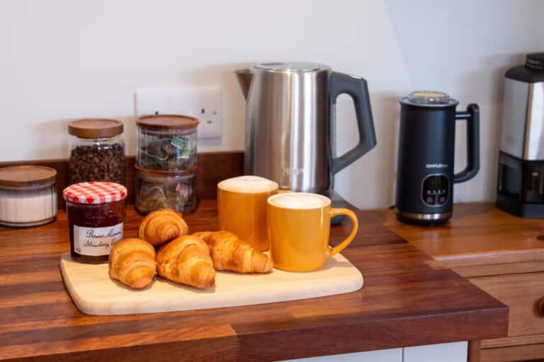 Tea and coffee station with a kettle, coffee machine, mugs and breakfast pastries