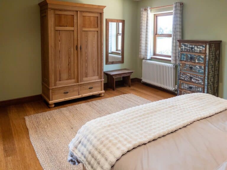 Main bedroom with a wooden wardrobe, dressing table and soft neutral bedding