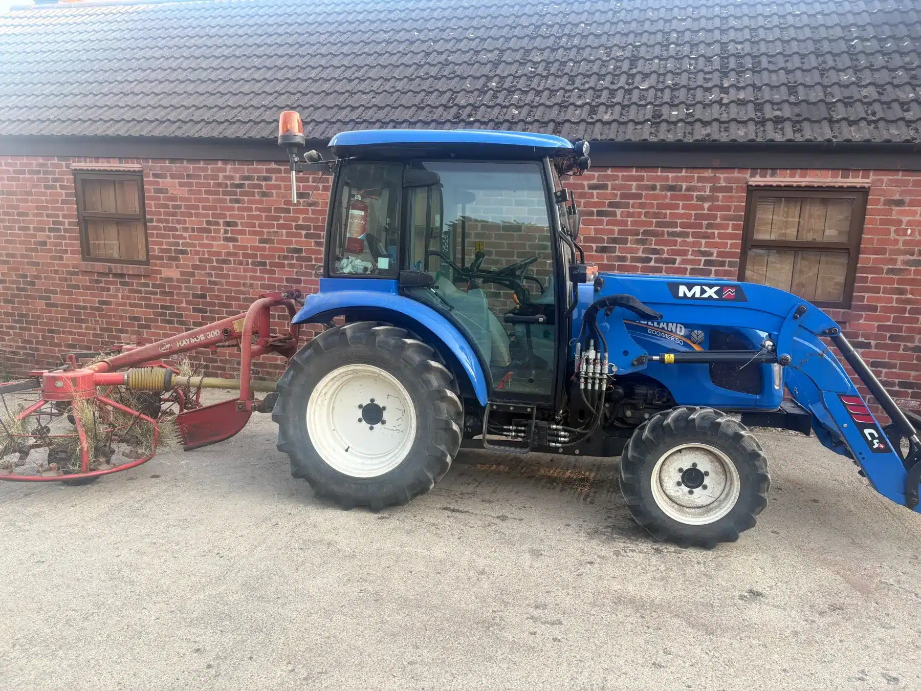 Little Blue, the New Holland Boomer tractor, with haymaking equipment beside a brick farm building